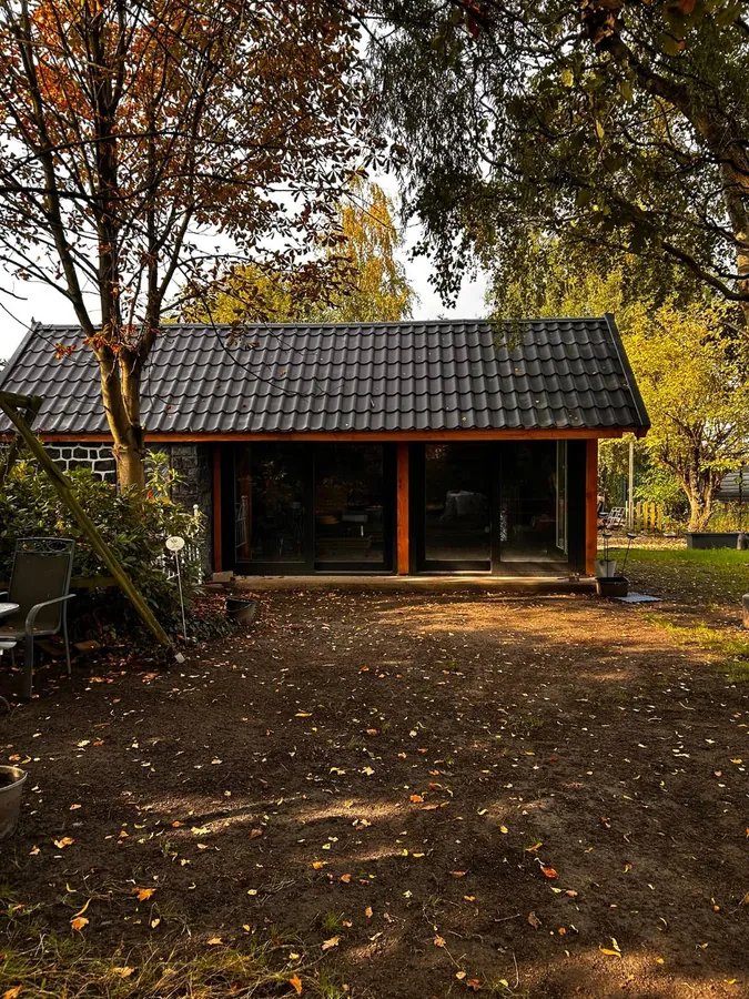 Het atelier vanaf de tuin, met zwart pannendak en houten staanders